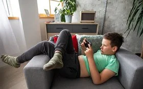 Ein Junge liegt mit einem Smartphone in der Hand auf einem Sessel.