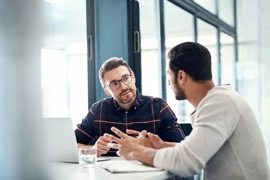 Zwei Männer sitzen im Gespräch in einem Büroraum.