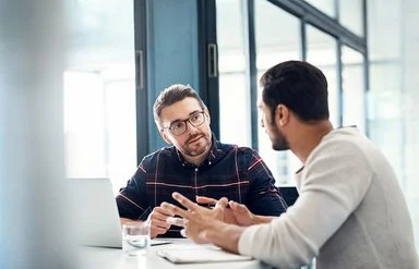 Zwei Männer sitzen im Gespräch in einem Büroraum.