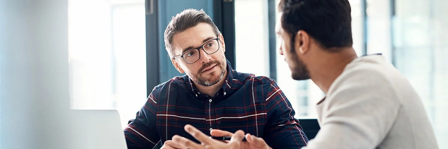 Zwei Männer sitzen im Gespräch in einem Büroraum.