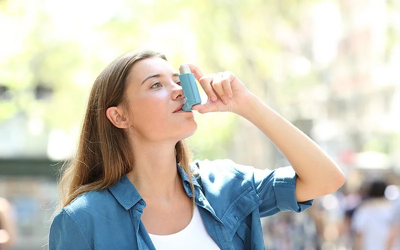 Eine junge Frau benutzt auf der Straße ein Asthmaspray.