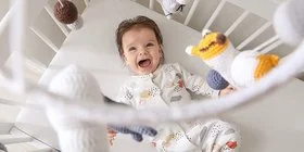 Fröhliches kleines Baby, das auf hängendes Mobile in der Krippe schaut.