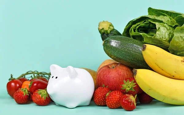 Ein kleines Sparschwein ist von gesundem Obst und Gemüse umgeben.