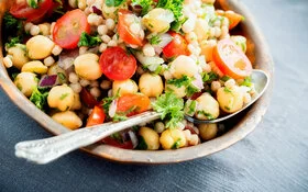 Ein Teller mit Couscous-Salat und Kirchererbsen steht auf einem gedeckten Tisch.