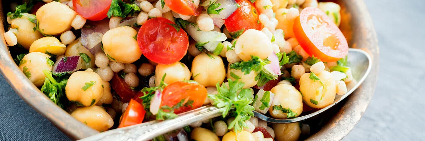 Ein Teller mit Couscous-Salat und Kirchererbsen steht auf einem gedeckten Tisch.