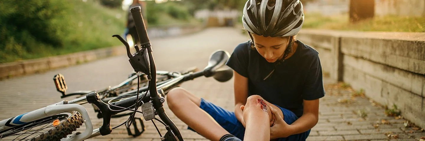 Hat er eine Tetanus-Impfung? Ein Junge ist mit dem Fahrrad gestürzt und schaut sich die Wunde am Knie an.