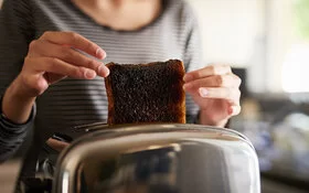 Eine Frau holt eine verbrannte Scheibe Toastbrot aus dem Toaster.
