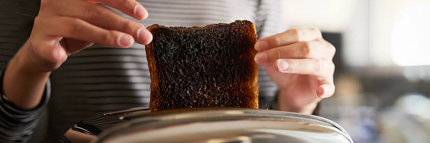 Eine Frau holt eine verbrannte Scheibe Toastbrot aus dem Toaster.