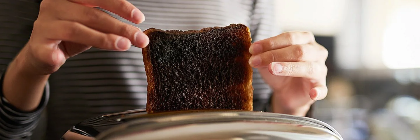 Eine Frau holt eine verbrannte Scheibe Toastbrot aus dem Toaster.