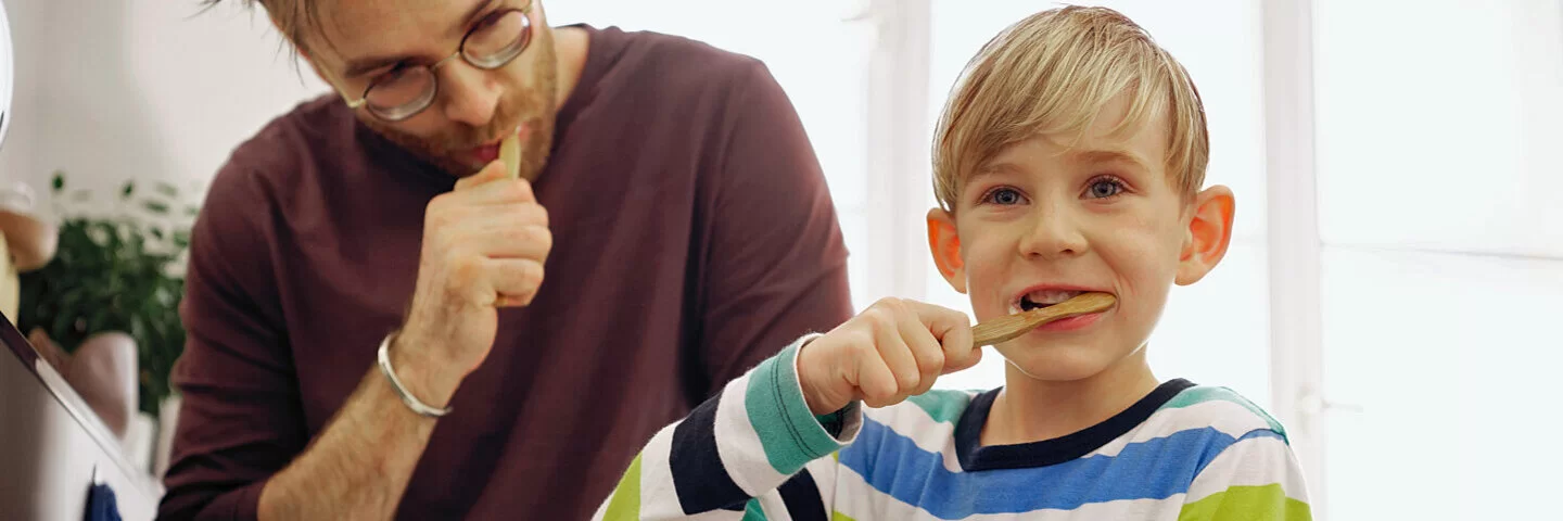 Ein Kind putzt mit seinem Vater Zähne, um Kreidezähne zu vermeiden.