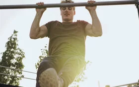 Ein junger Mann trainiert mit Klimmzügen seine Muskeln und stärkt damit seine Gesundheit.