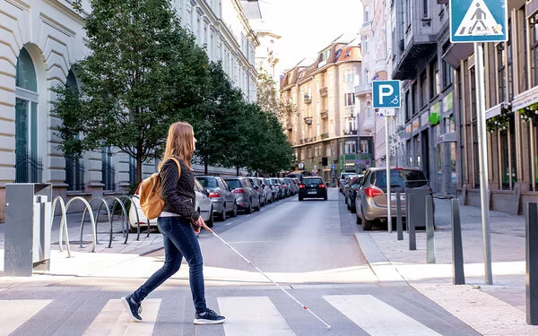 Frau mit Blindenstock kreuzt sicher eine Straße auf dem Zebrastreifen in der Innenstadt.