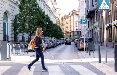 Frau mit Blindenstock kreuzt sicher eine Straße auf dem Zebrastreifen in der Innenstadt.