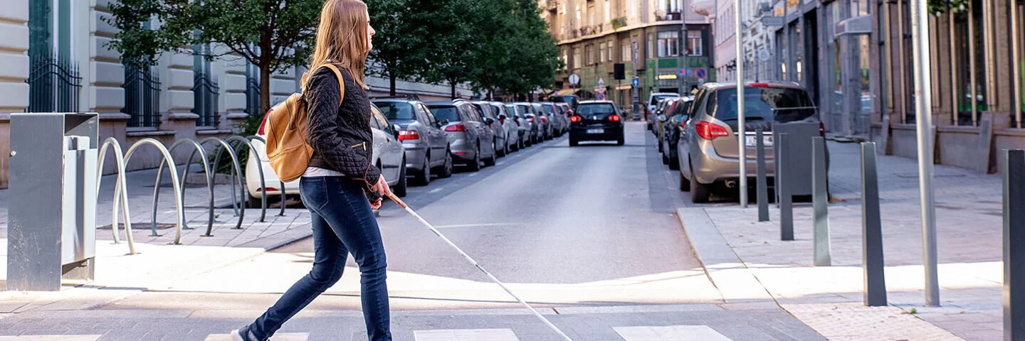Frau mit Blindenstock kreuzt sicher eine Straße auf dem Zebrastreifen in der Innenstadt.