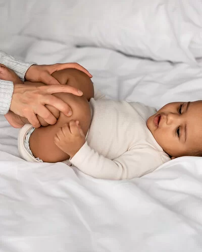 Eine Mutter macht Hüft-Gymnastik mit ihrem Baby, das auf dem Bett liegt.
