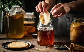 Eine Person entnimmt aus einem großen Glasgefäß die Pilzkultur zum Fermentieren.