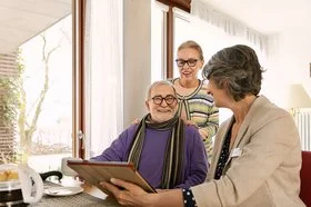 Ein altes Paar spricht mit einer Pflegeberaterin. Die Pflegeberaterin erklärt in einem Beratungsgespräch, wie sich die Pflege organisieren lässt.