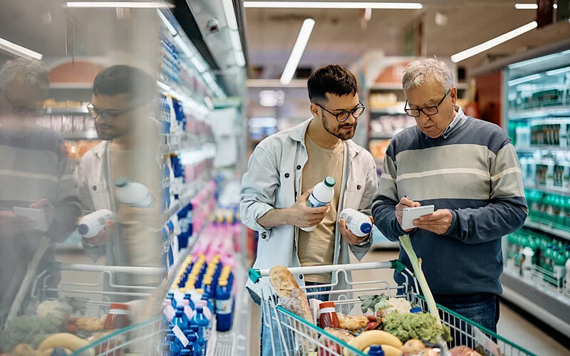 Ein junger Erwachsener und sein Vater möchten bewusst gesund einkaufen und halten sich daher an einen Einkaufszettel.