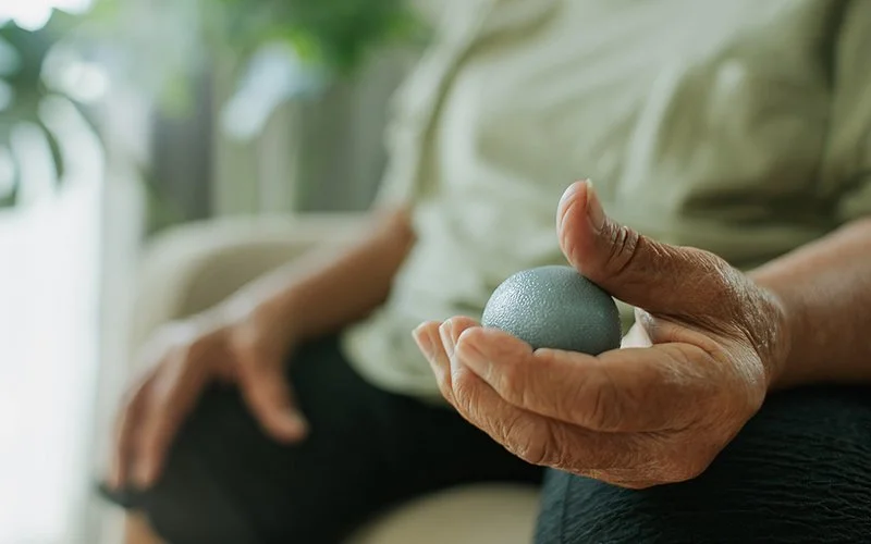 Therapieball in der Hand eines älteren Mannes.