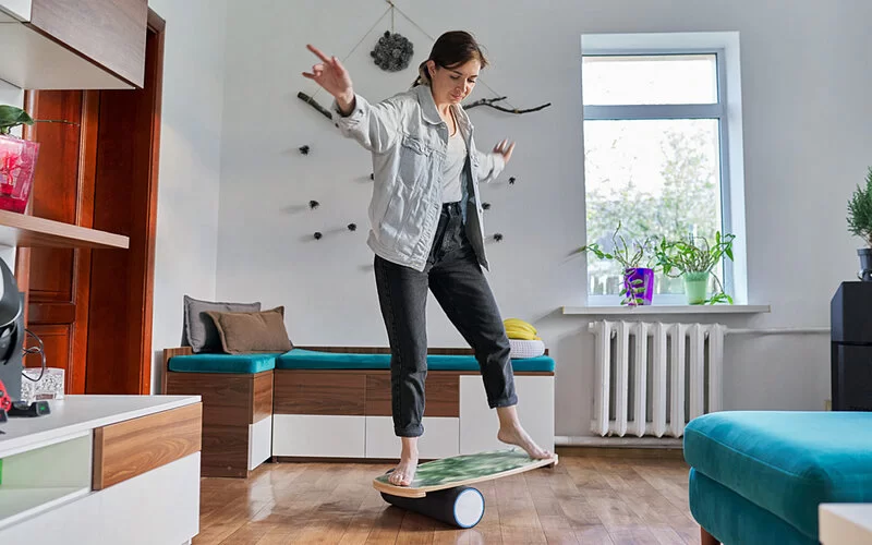Eine Frau steht auf einem surfbrettähnlichen Balance-Board und trainiert ihr Gleichgewicht.