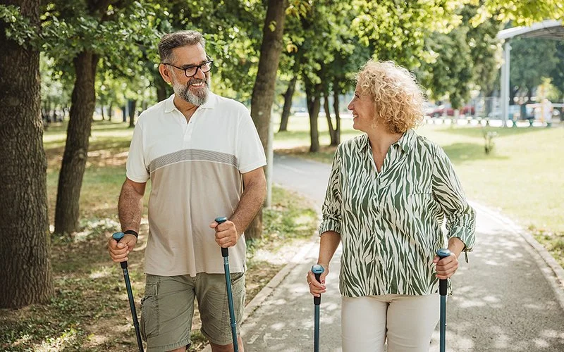 Eine Frau und ein Mann machen Nordic Walking und sehen sich dabei lächelnd an.