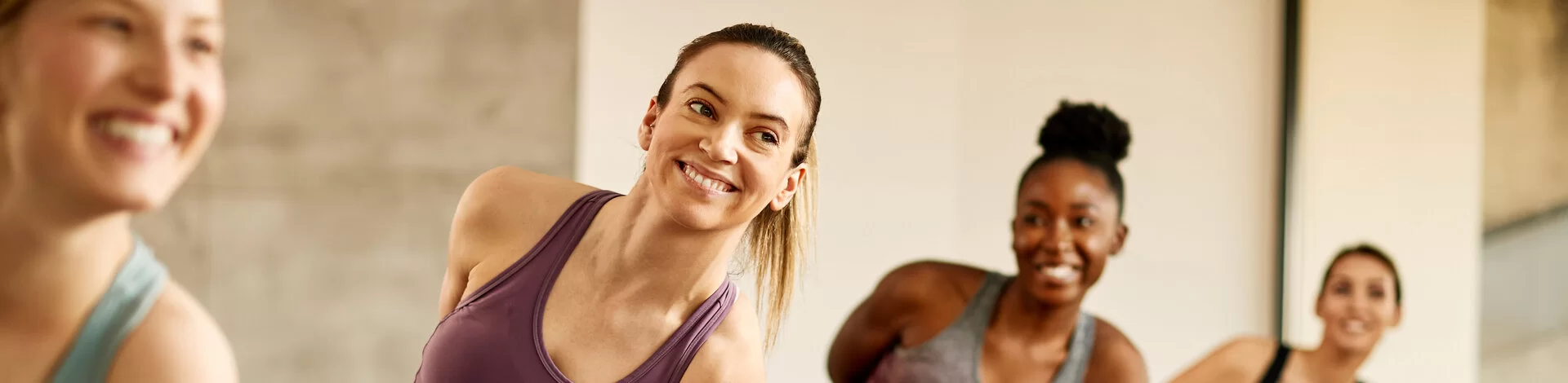 Mehrere Frauen trainieren zusammen in einem Yoga-Kurs. Sie stehen in einer Yoga-Haltung auf ihren Matten.