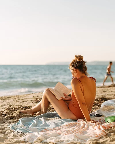 Eine Frau sitzt am Strand in der Sonne und liest ein Buch.
