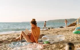 Eine Frau sitzt am Strand in der Sonne und liest ein Buch.