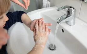 Eine Mutter hilft ihrem Sohn beim Händewaschen am Waschbecken.
