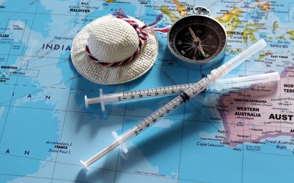Zwei Reiseimpfungen in Spritze auf einem Atlas, in Höhe von Australien liegend, mit Mini-Reiseaccessoires