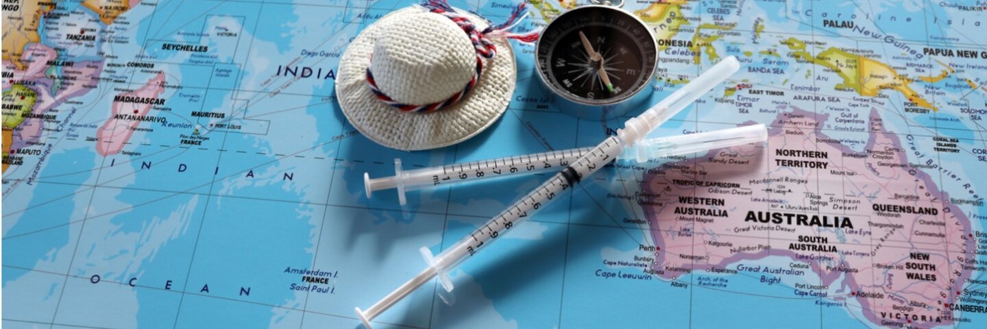Zwei Reiseimpfungen in Spritze auf einem Atlas, in Höhe von Australien liegend, mit Mini-Reiseaccessoires
