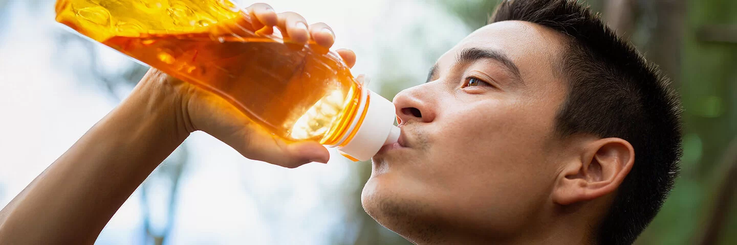 Ein junger Mann trinkt im Freien aus einer durchsichtigen, orangefarbenen Trinkflasche.