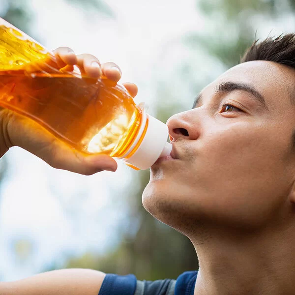 Ein junger Mann trinkt im Freien aus einer durchsichtigen, orangefarbenen Trinkflasche. 