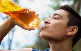 Ein junger Mann trinkt im Freien aus einer durchsichtigen, orangefarbenen Trinkflasche. 