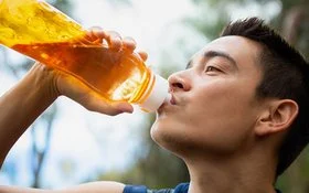 Ein junger Mann trinkt im Freien aus einer durchsichtigen, orangefarbenen Trinkflasche.