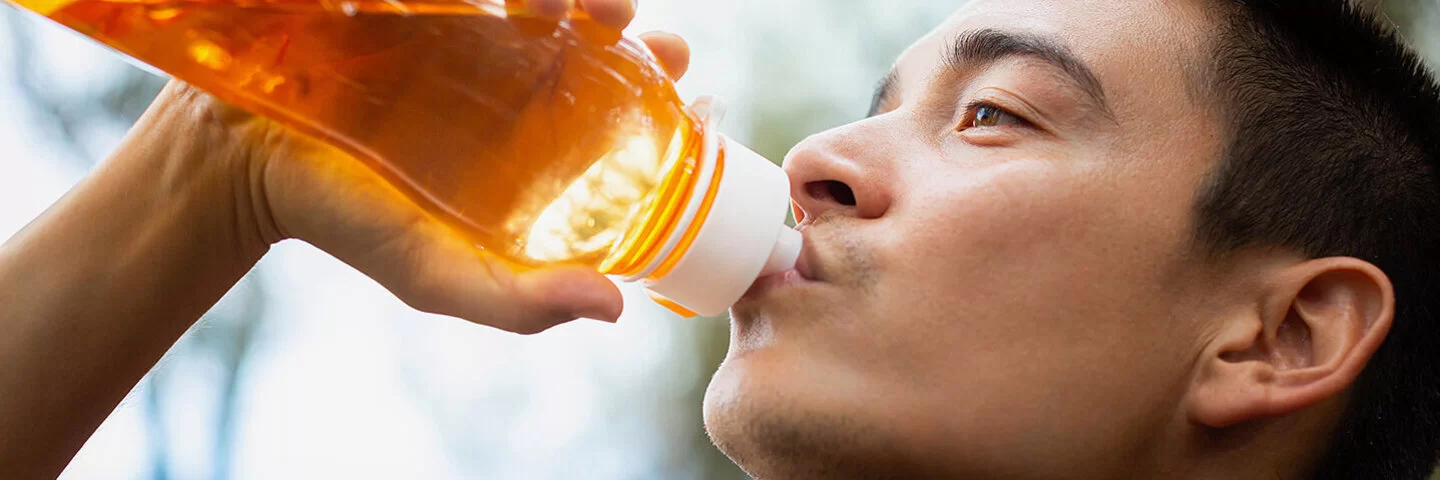 Ein junger Mann trinkt im Freien aus einer durchsichtigen, orangefarbenen Trinkflasche.