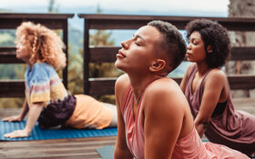 Drei Frauen machen zusammen Yoga auf einer Veranda.