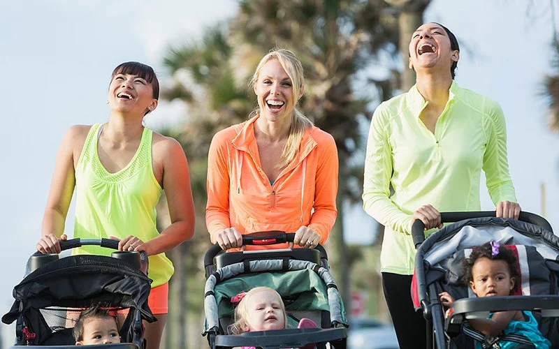 Drei junge Mütter gehen mit einem Baby-Jogger und ihren Kindern laufen.