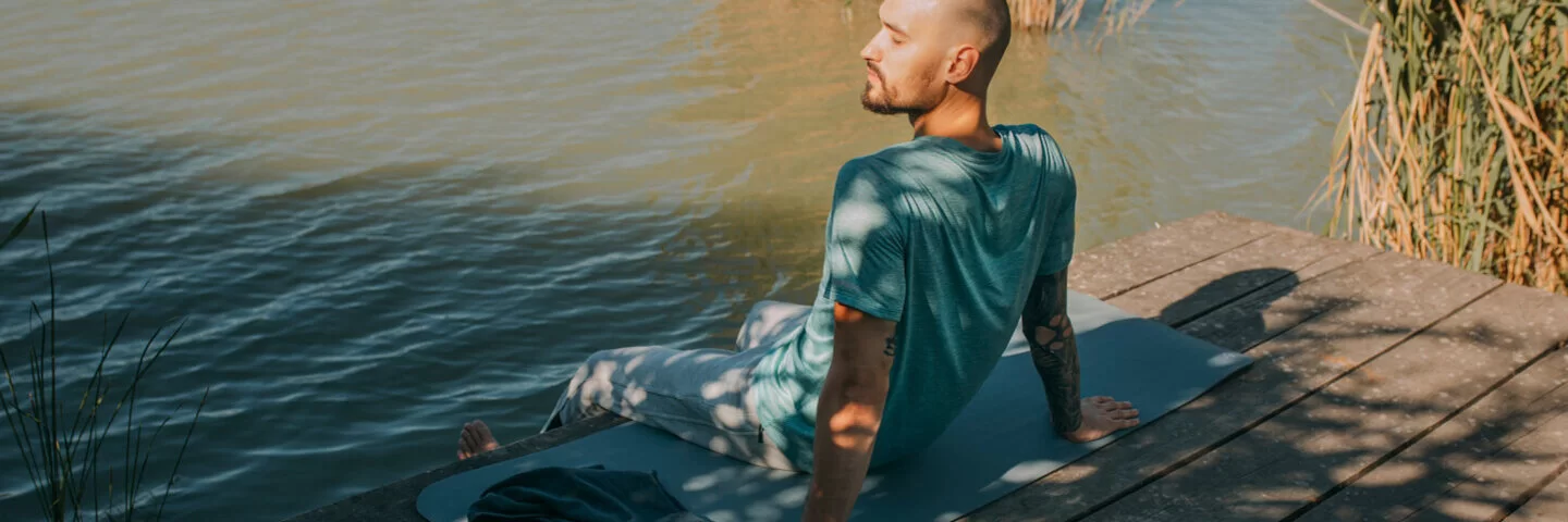 Ein Mann führt auf seiner Yogamatte am Wasser eine Achtsamkeitsübung zur Krebsbewältigung durch.