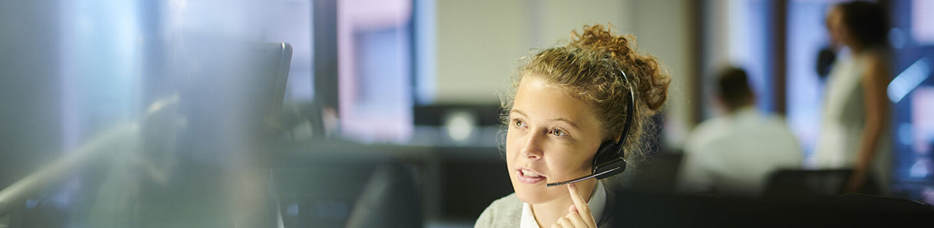 Eine Frau sitzt mit einem Headset vor einem Computerbildschirm und telefoniert.