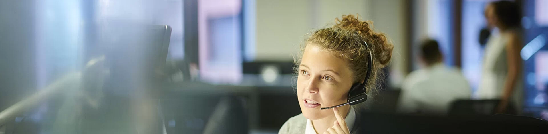 Eine Frau sitzt mit einem Headset vor einem Computerbildschirm und telefoniert.