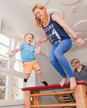 Ein junges Mädchen und ein Kleinkind springen Hand in Hand von einem Sportgerät und lachen.