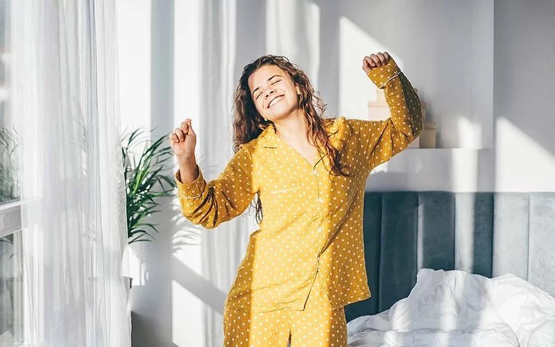 Eine Frau im gelben Pyjama tanzt in ihrem Schlafzimmer.