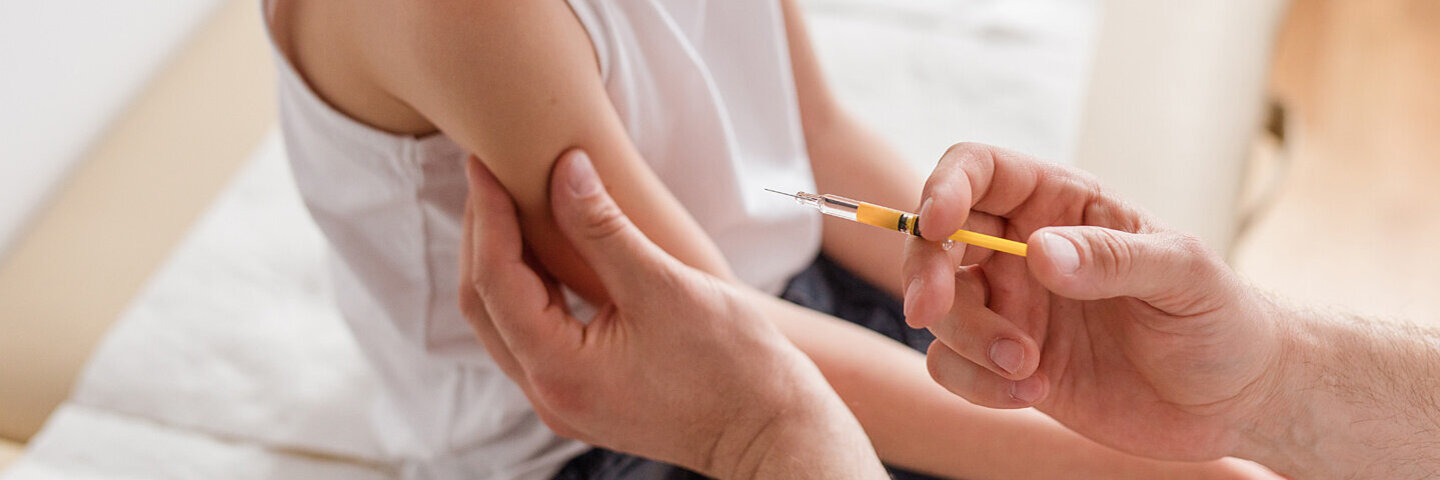 Ein blondes Mädchen bekommt vom Arzt für die Kinderimpfung eine Spritze in den Arm gestochen.