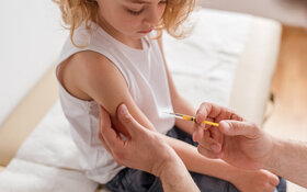Ein blondes Mädchen bekommt vom Arzt für die Kinderimpfung eine Spritze in den Arm gestochen.