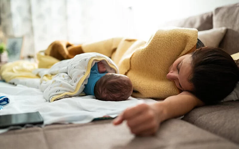 Eine Mutter liegt mit ihrem Baby auf der Couch und ruht sich aus.