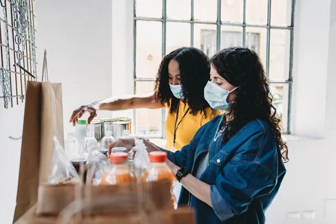 Zwei Frauen, gekleidet in den Farben der Ukraine, verpacken Lebensmittel als Hilfe für Flüchtlinge.