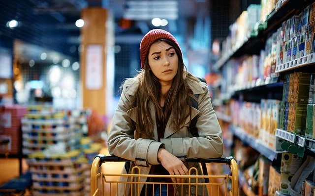 Eine Frau schiebt einen Einkaufswagen und schaut kritisch auf die Supermarktregale.