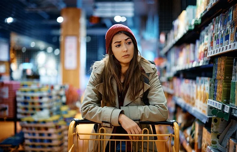 Eine Frau schiebt einen Einkaufswagen und schaut kritisch auf die Supermarktregale.