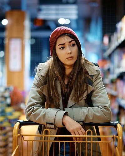 Eine Frau schiebt einen Einkaufswagen und schaut kritisch auf die Supermarktregale.